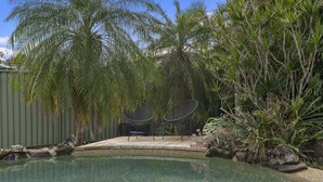 Una piscina con dos sillas de descanso, rodeada de palmeras y diversas plantas.