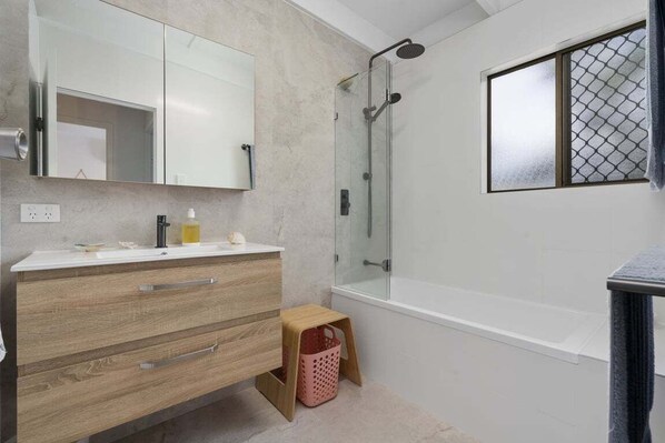 A modern bathroom with a glass shower enclosure, a white bathtub, and a wooden vanity with drawers.