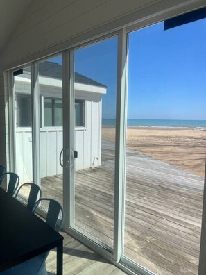 Una habitación con un amplio ventanal corredera que da a una terraza de madera con vistas a una playa.