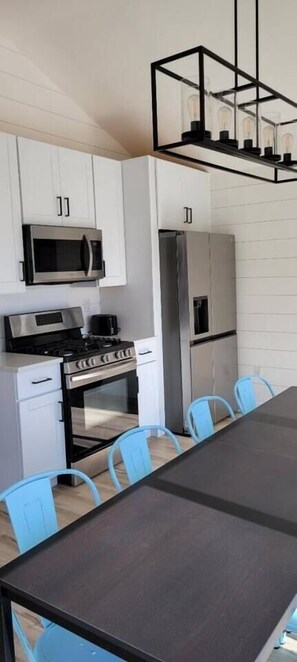 Una cocina moderna con armarios blancos, electrodomésticos de acero inoxidable y una mesa de comedor con sillas azules.