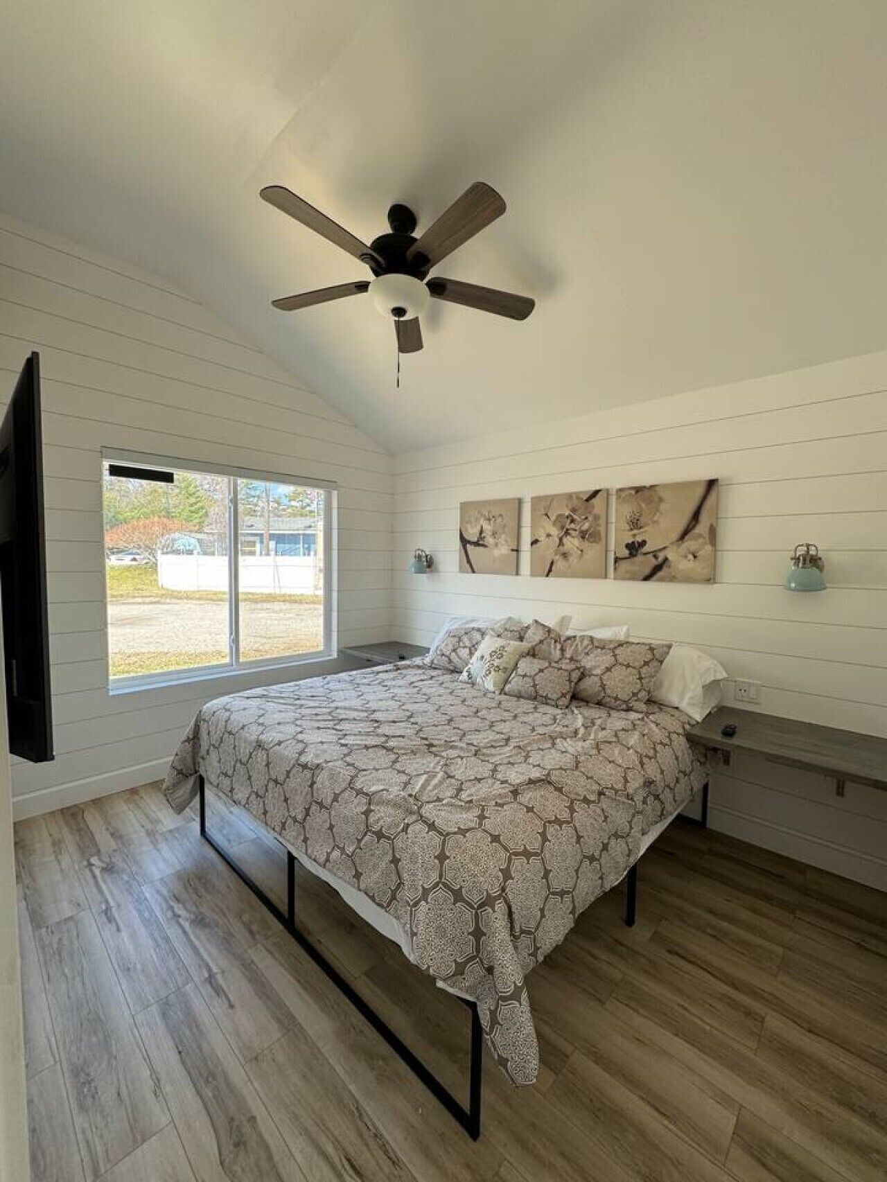 Ein Schlafzimmer mit einem Bett, einem Deckenventilator, einem Fenster und Kunstwerken an der Wand.