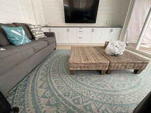 A living room with a sofa, two wicker ottomans, a patterned rug, and a television mounted on the wall.