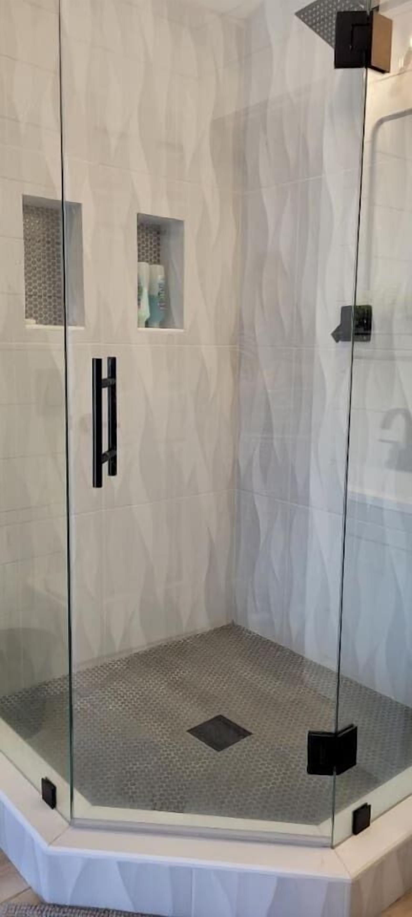 Una cabina doccia in vetro con parete strutturata, un pannello di controllo e un piccolo ripiano.
