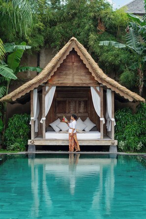 A wooden structure with a thatched roof and white curtains, overlooking a pool. - Villa Tigapuluh (Seminyak)