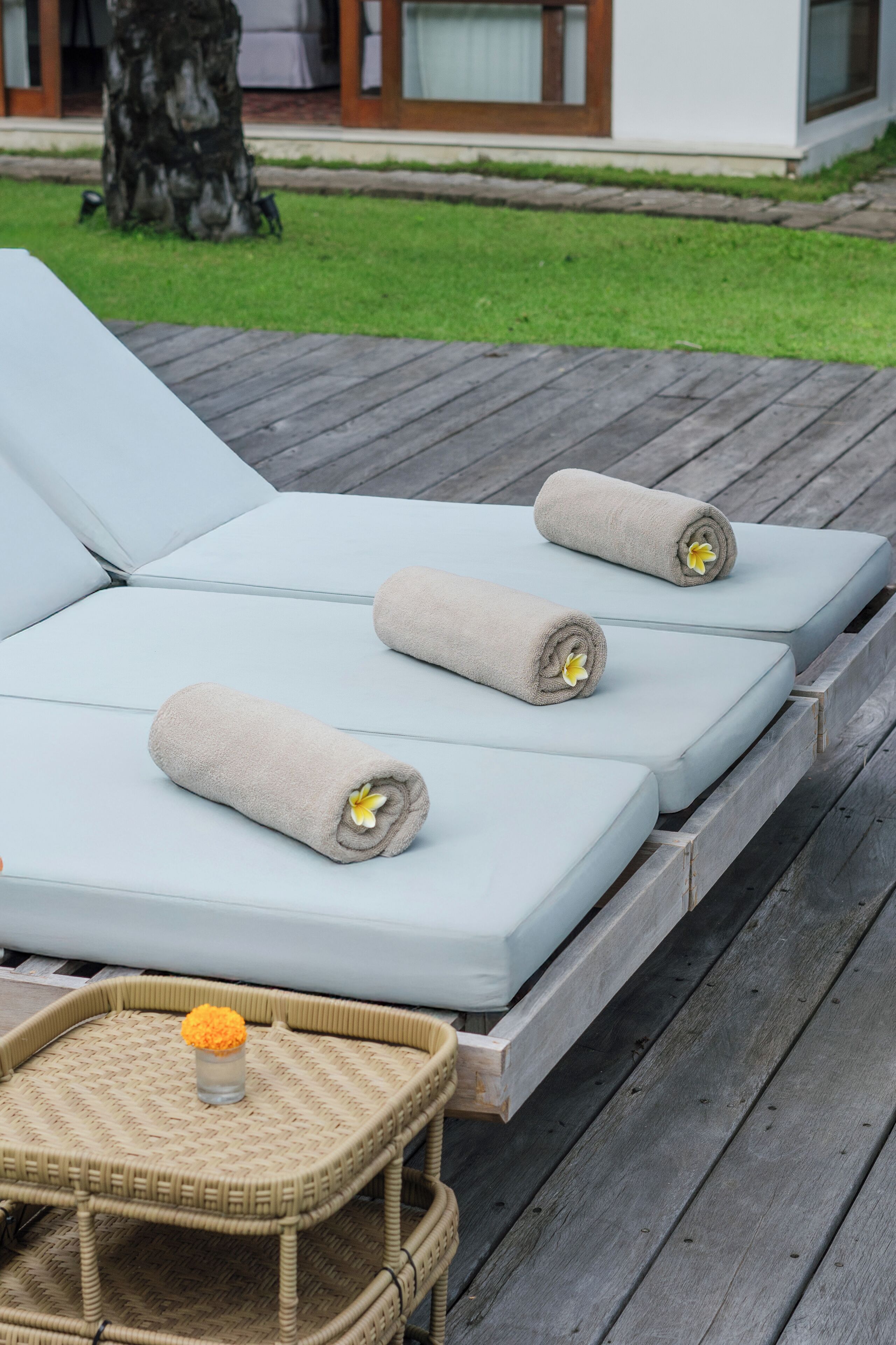 Un ensemble de fauteuils de jardin bleu clair, accompagnés de serviettes beige et de fleurs jaunes, disposés sur une terrasse en bois.