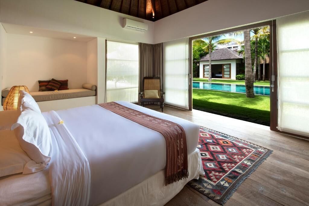A bedroom with a large bed, a chair, and a view of a swimming pool.