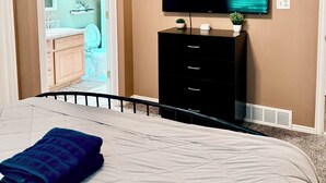 Ein Schlafzimmer mit Bett, Wandfernseher, Kommode und Deckenventilator.