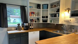 A modern kitchen with dark cabinets, a wooden countertop, and a built-in dishwasher. Shelves above the sink hold various kitchen items, and a window with curtains is visible. - Wolf Creek Basecamp - Premier fishing! Walking distance to restaurants and bars (Wolf Creek)