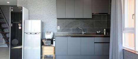 Una cocina moderna con armarios grises, un refrigerador de acero inoxidable, un microondas y un lavamanos.