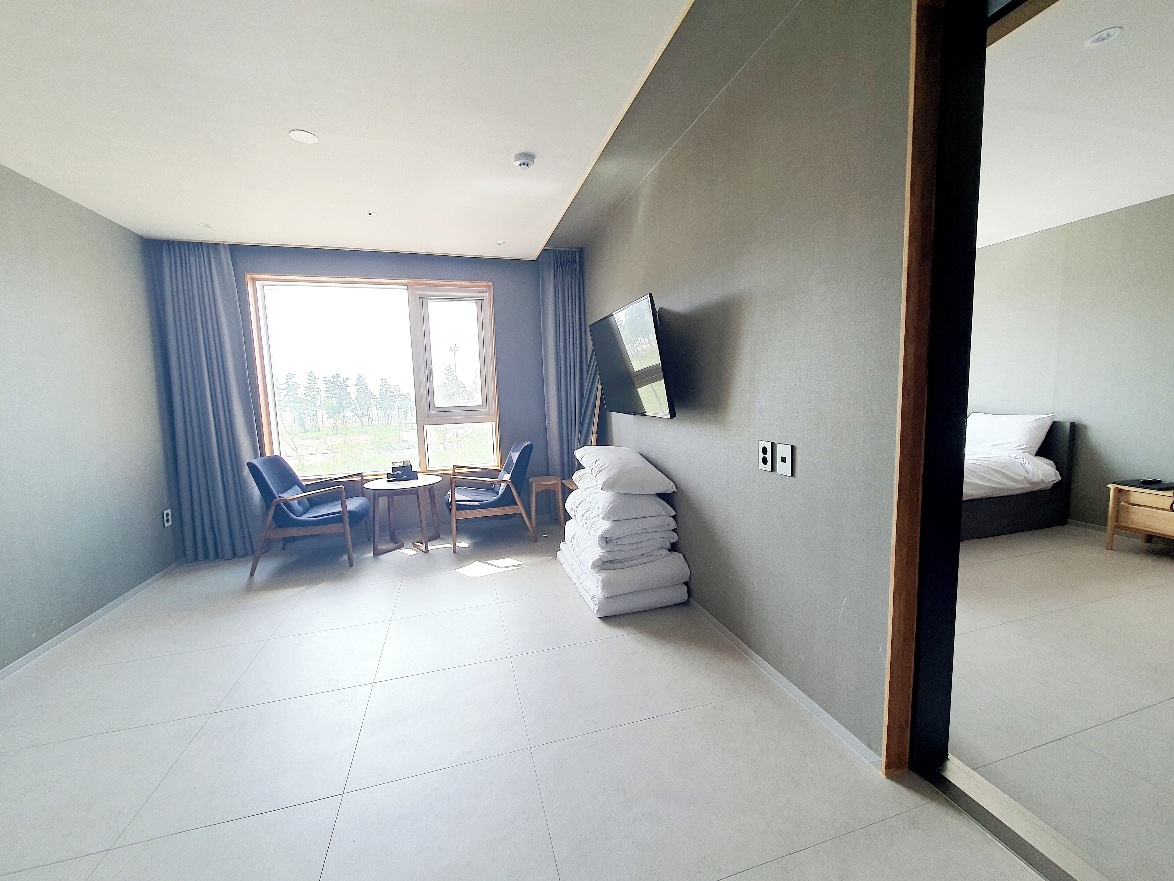 A hotel room with a bed, a TV mounted on the wall, a desk with a chair, and a window with curtains.