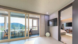Une chambre d’hôtel moderne dotée d’une grande porte-fenêtre coulissante donnant sur un balcon, d’un téléviseur à écran plat fixé au mur et d’un grand miroir rond posé sur le sol.