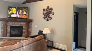 A living room with a fireplace, a ceiling fan, a TV, and a decorative wall piece. - Superb 5-bedroom house in Big Lake in friendly, safe neighborhood. (Big Lake)