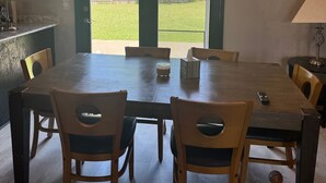 A dining area with a large wooden table, four chairs, a chandelier, and a view of a backyard through a glass door. - Superb 5-bedroom house in Big Lake in friendly, safe neighborhood. (Big Lake)