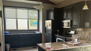 A kitchen with dark cabinets, a stainless steel refrigerator, a microwave, and a large window. - Superb 5-bedroom house in Big Lake in friendly, safe neighborhood. (Big Lake)
