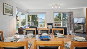 Un coin repas avec une table dressée pour quatre personnes, un téléviseur et une vue sur l’extérieur.