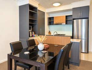 A modern kitchen with a built-in microwave, stainless steel refrigerator, and a dining area with a glass table and black chairs.