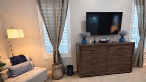 Ein Wohnzimmer mit einer Couch, einem Fernseher auf einer Holzkommode und einer Lampe.