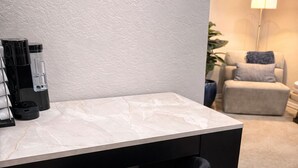 Ein moderner Büroraum mit einem Marmortisch, einem schwarzen Stuhl mit goldfarbenen Beinen und einer Kaffeemaschine.