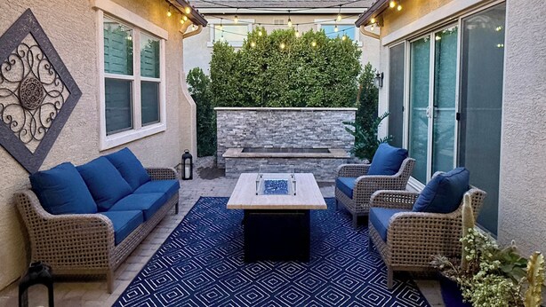 Ein Terrassenbereich im Freien mit einer Steinmauer, einem blauen Teppich mit Muster, Korbmöbeln und Lichterketten.