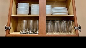 Ein Holzschrank mit Regalen, auf denen weiße Teller und klare Gläser stehen.