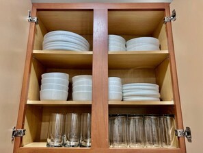 Ein Holzschrank mit Regalen, auf denen weiße Teller und klare Gläser stehen.