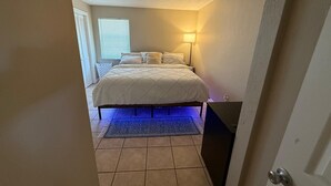 Une chambre à coucher avec un lit, une table de chevet, une lampe et une fenêtre avec des stores.