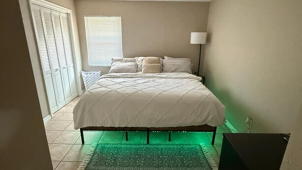 Une chambre à coucher avec un lit, une fenêtre avec des stores, une lampe et un tapis éclairé de lumière verte.