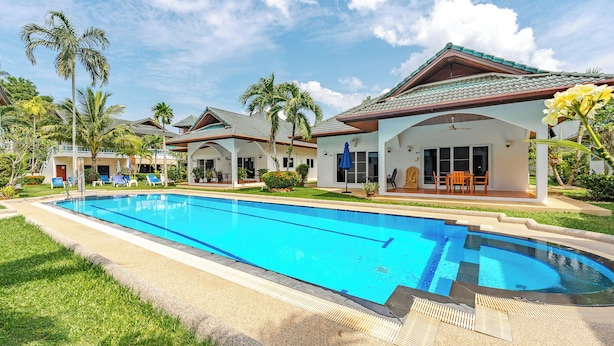 A swimming pool with lounge chairs, palm trees, and a building with a tiled roof. - IslandHideaway Near Promthep Sunset V205 (Rawai)