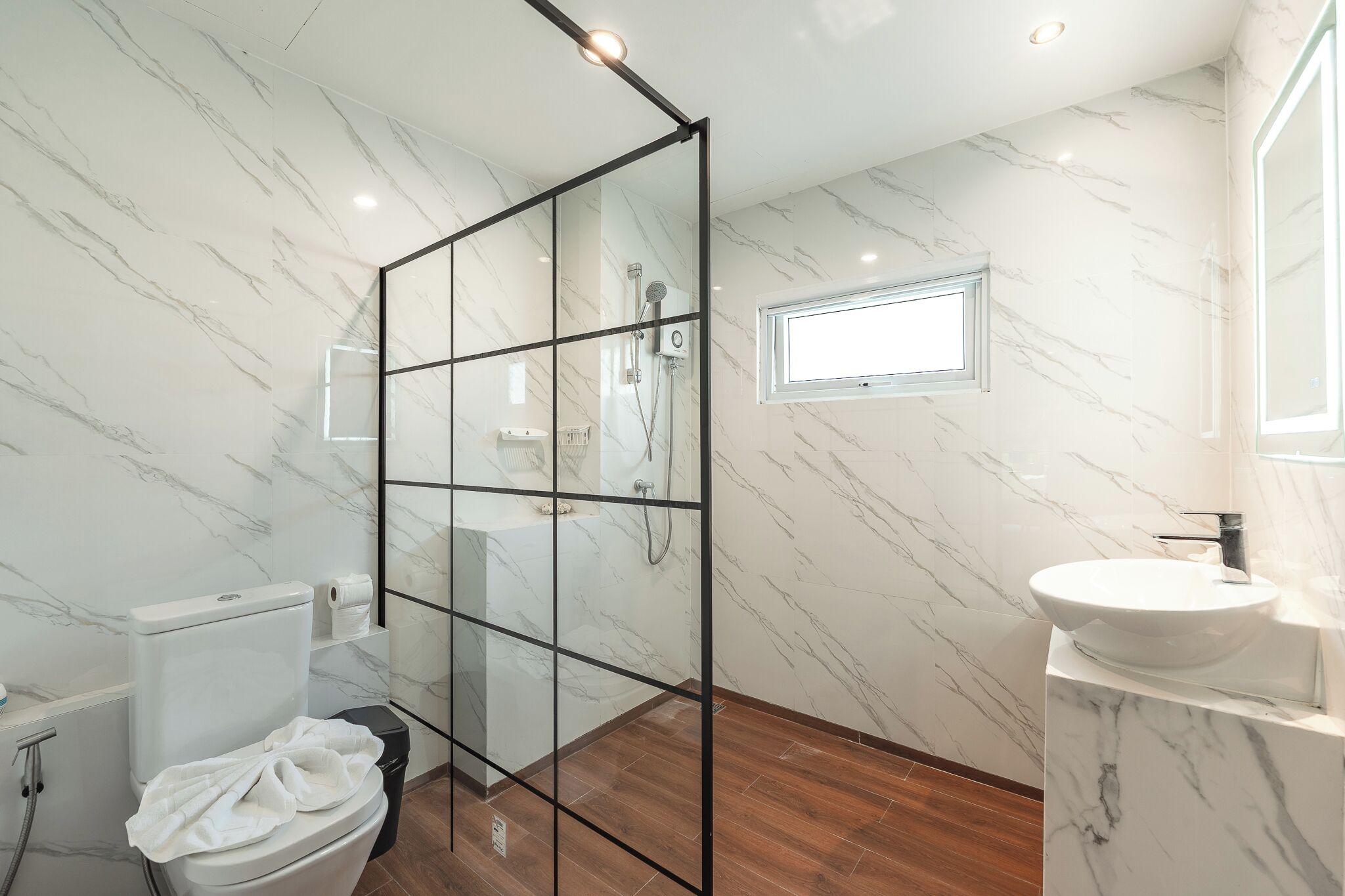 Een moderne badkamer met een douchecabine van glas, een wit toilet, een wastafel en een marmeren wand.