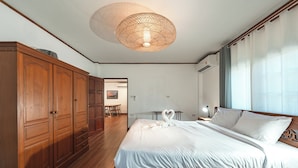 A bedroom with a wooden bed, a large wardrobe, a hanging light fixture, and a view of the outside through a window. - IslandHideaway Near Promthep Sunset V205 (Rawai)