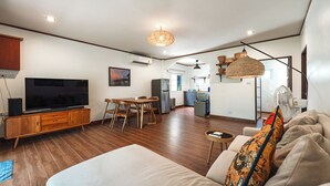 A modern living room with a flat-screen TV, wooden furniture, a dining area, and a kitchen in the background. - IslandHideaway Near Promthep Sunset V205 (Rawai)