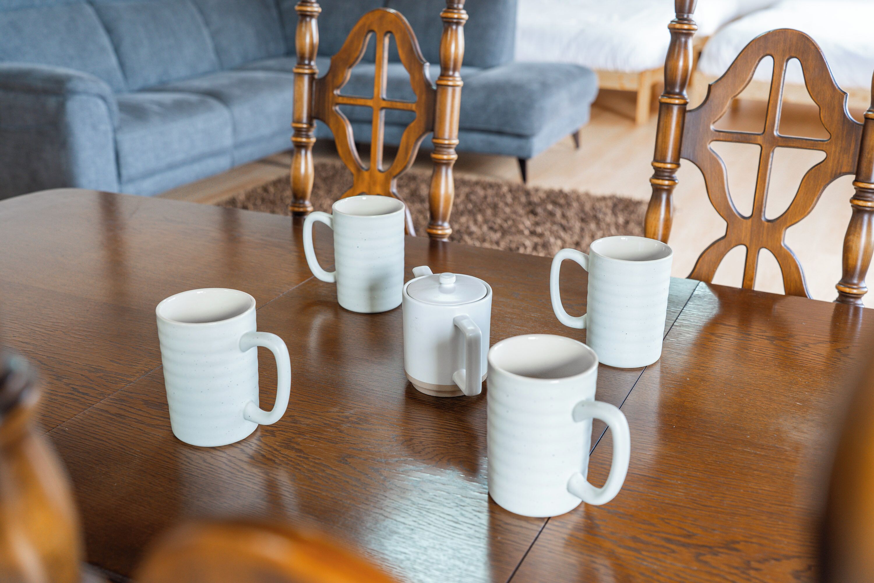 Una mesa de madera con seis tazas blancas de cerámica y una tetera.