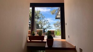Un interior moderno con techo de madera, un amplio ventanal corredero que da a un área exterior con mobiliario y plantas.