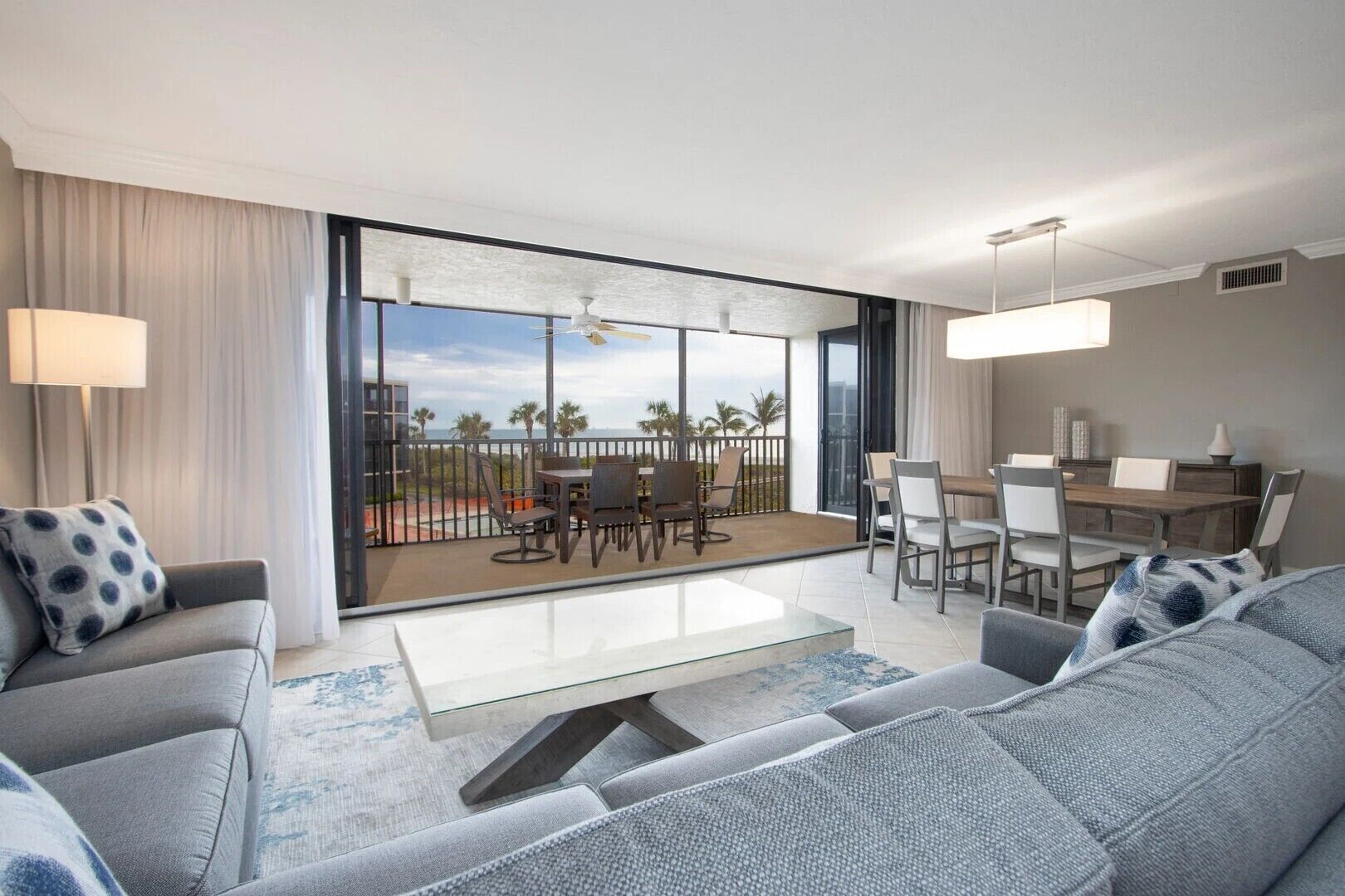 Una habitación de hotel moderna con balcón, zona de comedor y sala de estar con sofá y sillones.