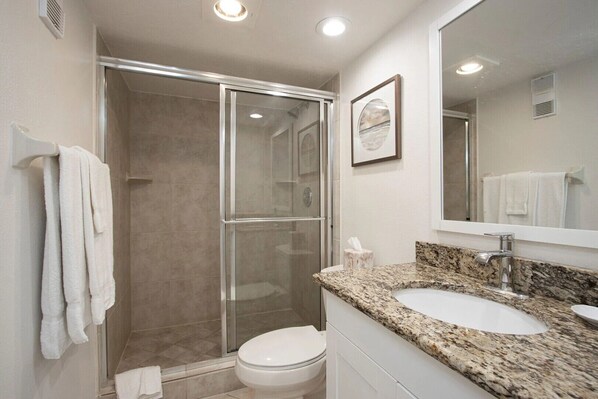 Un baño moderno con ducha envuelta en vidrio, inodoro blanco y lavamanos con encimera de granito.