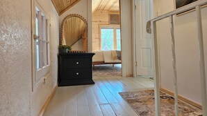 Kapea käytävä, jossa on puulattiat ja -seinät, johtaa makuuhuoneeseen, jossa on sänky ja ikkuna.