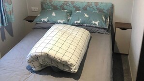 A neatly made bed with a checkered blanket, two pillows with a dog pattern, and a headboard with a leaf design.