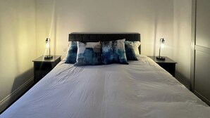Un letto rifatto con lenzuola bianche e cuscini a righe blu e bianche, affiancato da due comodini con lampade.