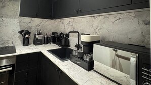 Una cucina moderna con mobili scuri, un piano di lavoro in marmo, una macchina da caffè e una lavastoviglie.