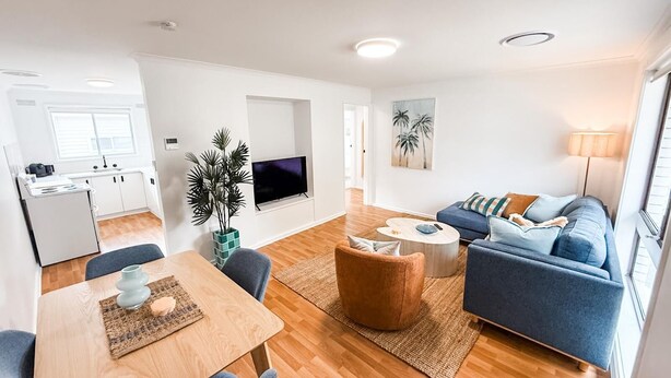 A modern living room with a sofa, coffee table, and a TV. There is a kitchen area with a fridge and a dining table. - 2/7 Halloran Street, Wagga Wagga (Wagga Wagga)