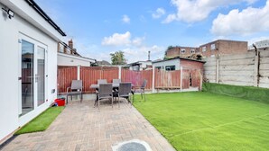 A patio with a table and chairs, a small grassy area, and a wooden fence.