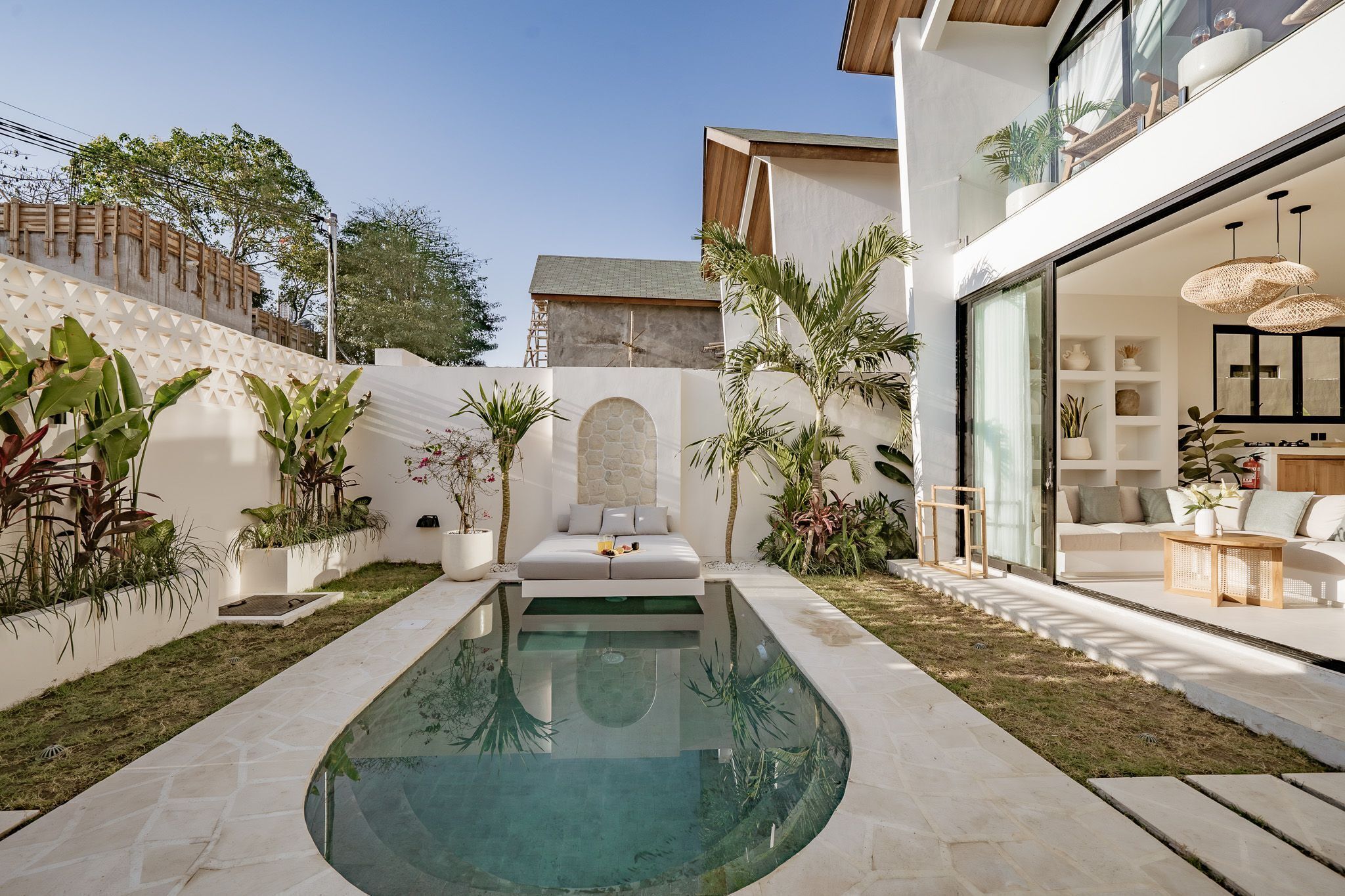 A modern outdoor pool area with a geometric pool design, surrounded by a white wall with a textured pattern and potted plants.