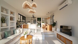 A modern living room with a sofa, coffee table, and TV. There are shelves with plants and decorative items. - Villa Yuni Uluwatu (Pecatu)