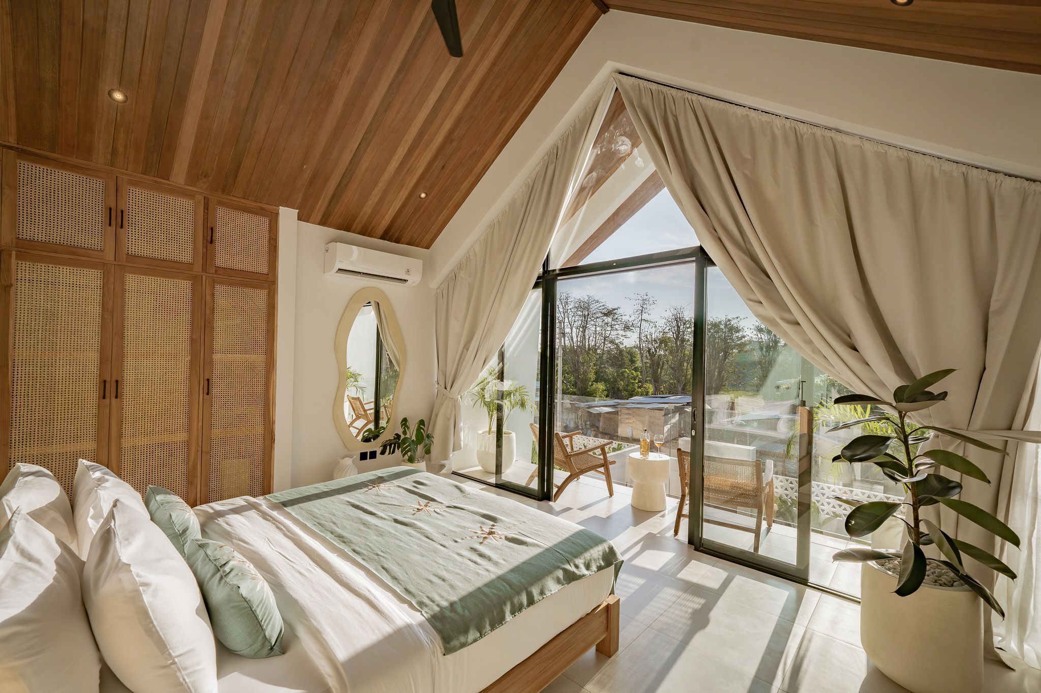 A bedroom with a large bed, a view of the outdoors, and a balcony with seating.