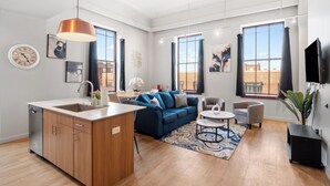 A modern living space with a kitchen, a blue sofa, a dining area, and large windows offering views of the city. - Stylish Loft in St. Louis with Gym, Rooftop, Free Gated Parking, and Pool (St. Louis)