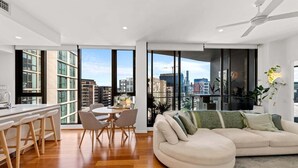 A modern apartment with a kitchen, dining area, and living room with large windows offering city views. - Modern Panoramic Luxury in Fortitude Valley (Brisbane)