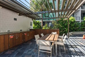 Une terrasse extérieure avec une table et des chaises en bois, un bar intégré et une structure en forme de pergola.