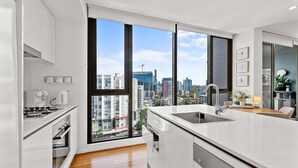 A modern kitchen with a large window, white cabinetry, and a view of a cityscape. - Modern Panoramic Luxury in Fortitude Valley (Brisbane)