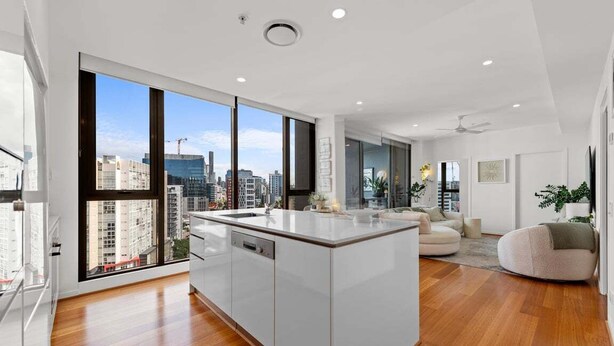 A modern apartment with a large kitchen island, a dining area, and a living room with a view of the city skyline. - Modern Panoramic Luxury in Fortitude Valley (Brisbane)