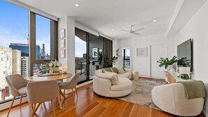 A modern living room with a large window, a dining area, and a seating area with a sofa and chairs. - Modern Panoramic Luxury in Fortitude Valley (Brisbane)